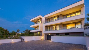 A multi-story modern building with balconies, a paved courtyard, and a staircase leading to the entrance.