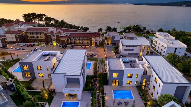 A modern hotel complex with multiple buildings, rooftop pools, and a view of the sea at sunset.