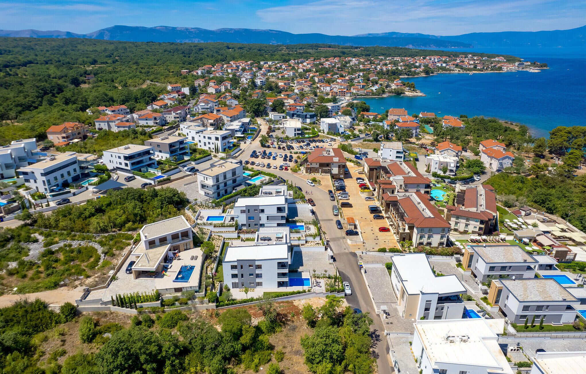 Vista aérea de una zona residencial costera con edificios modernos, un puerto deportivo y una vista despejada del mar.