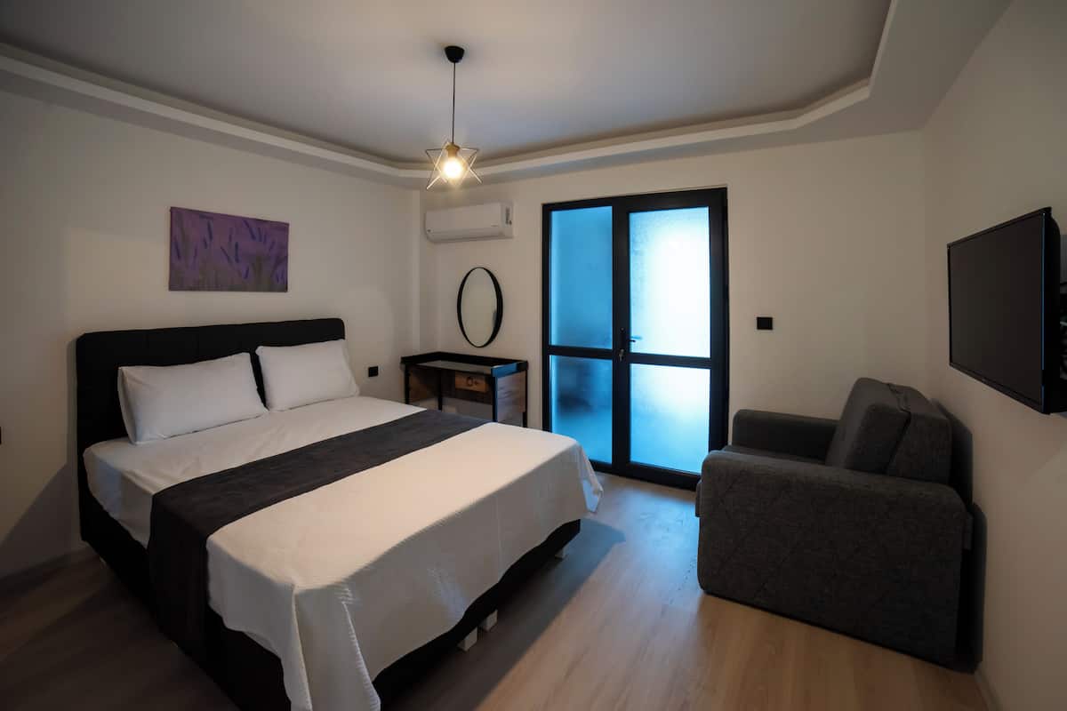 A modern bedroom with a large bed, a bedside table, a chair, a TV, and a window with a view.