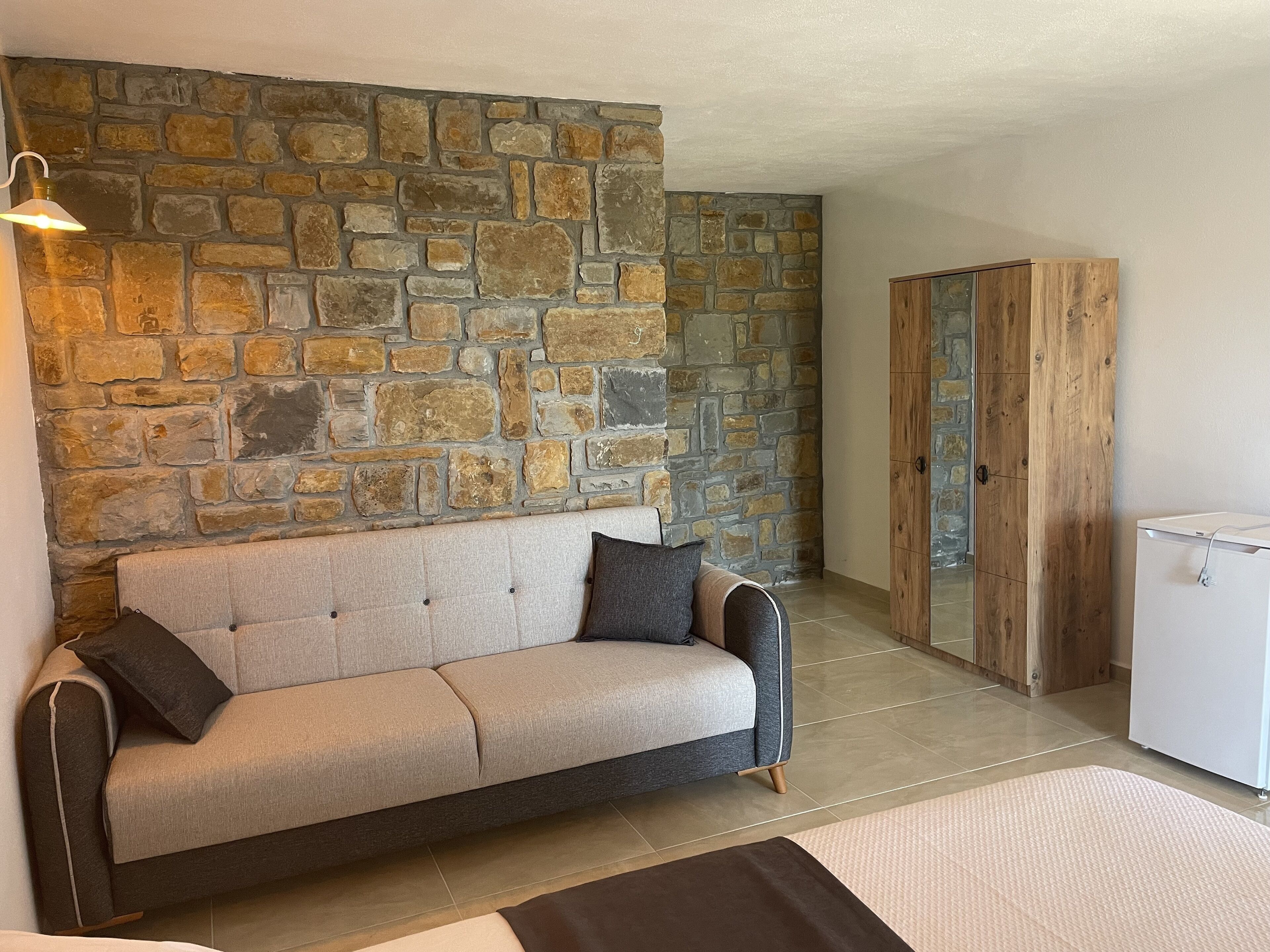 Una sala de estar con pared de piedra, un sofá, un armario de madera y un electrodoméstico blanco.