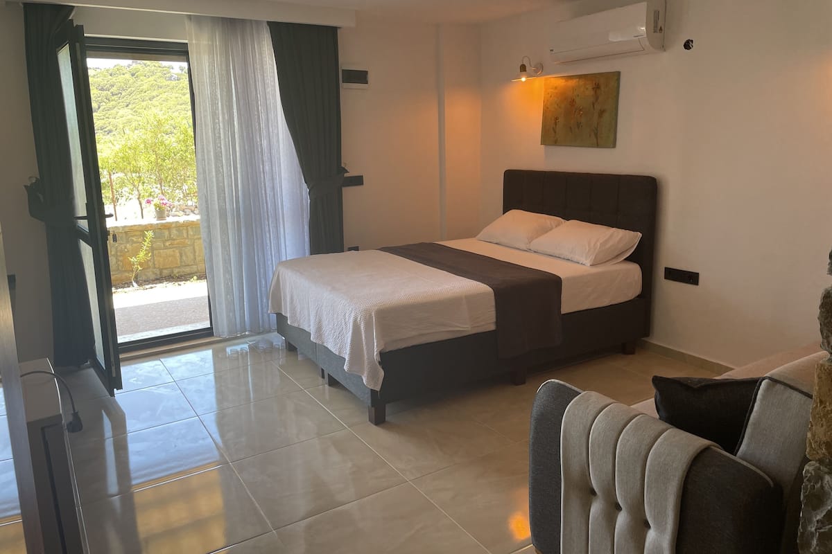 A bedroom with a bed, a chair, a window with curtains, and an air conditioning unit.