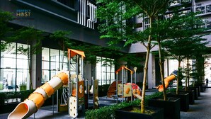 Un parque infantil interior con toboganes y estructuras para escalar, rodeado de plantas en macetas y árboles.