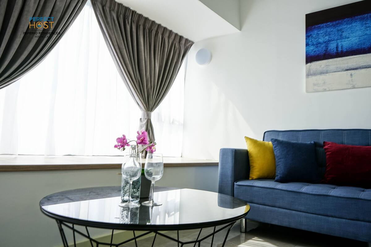 Uma sala de estar moderna com um sofá azul, uma mesa de centro de vidro e uma pintura na parede.