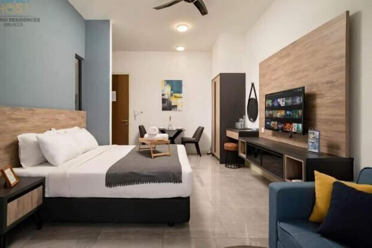 Quarto de hotel com cama, escrivaninha, televisão e área de estar.
