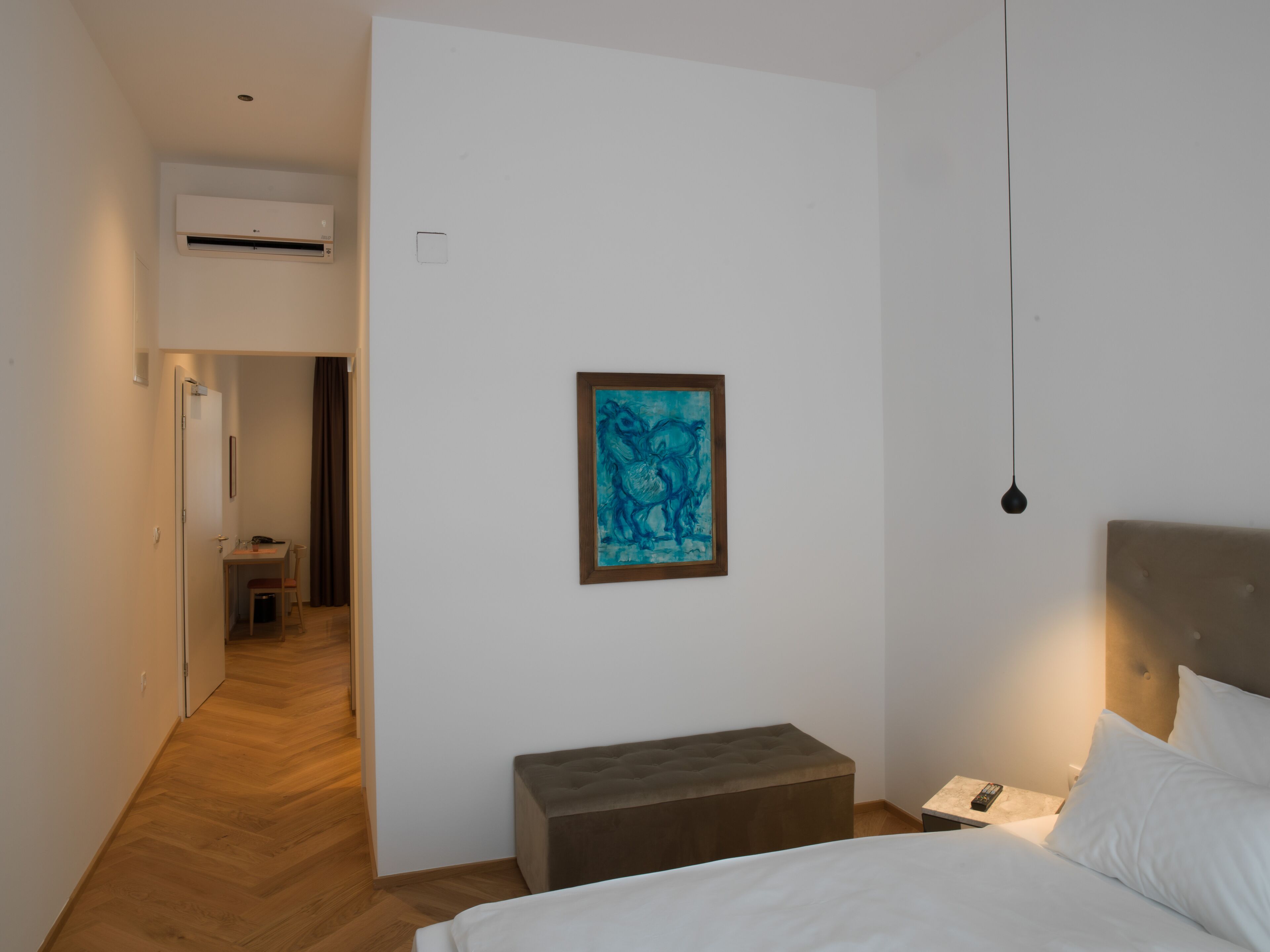Una habitación de hotel con una cama, una mesita de noche, un banco y un cuadro en la pared.