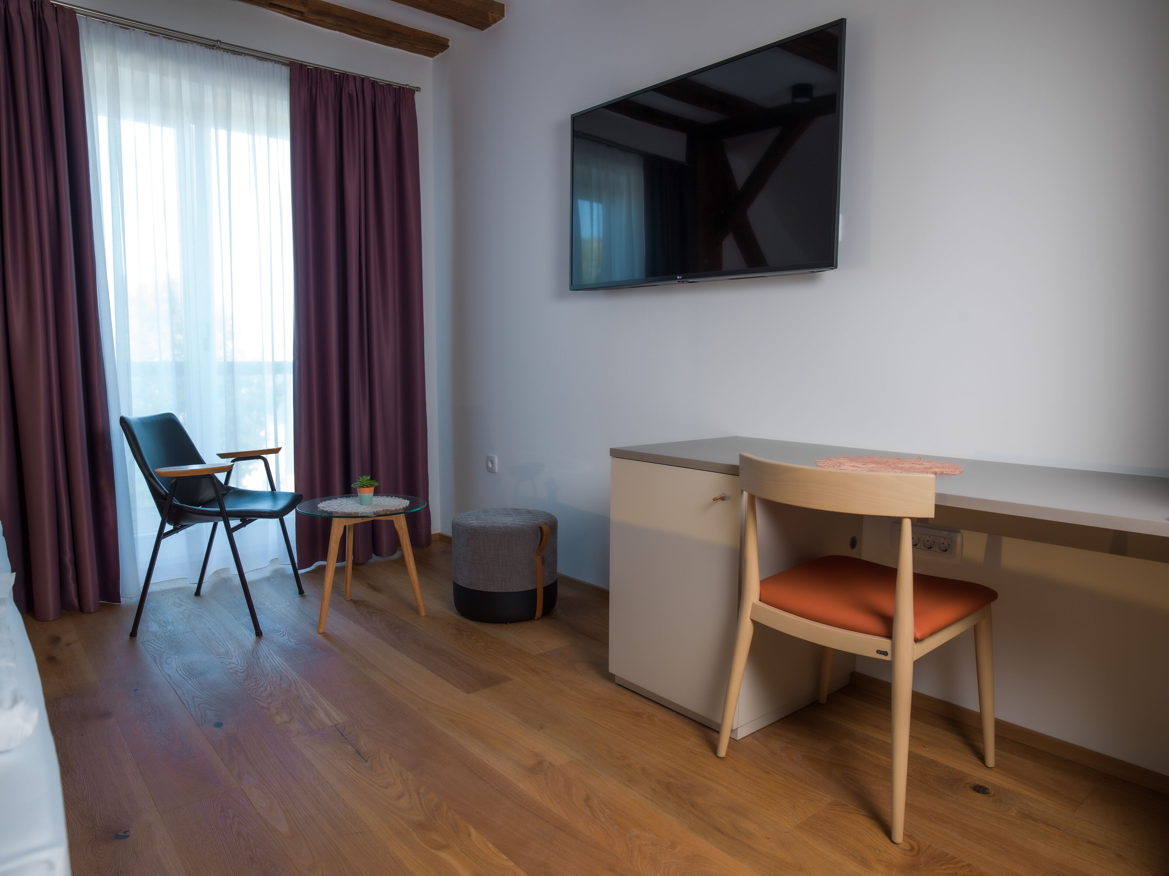 Una habitación con cama, escritorio, silla, televisor y ventana con cortinas.