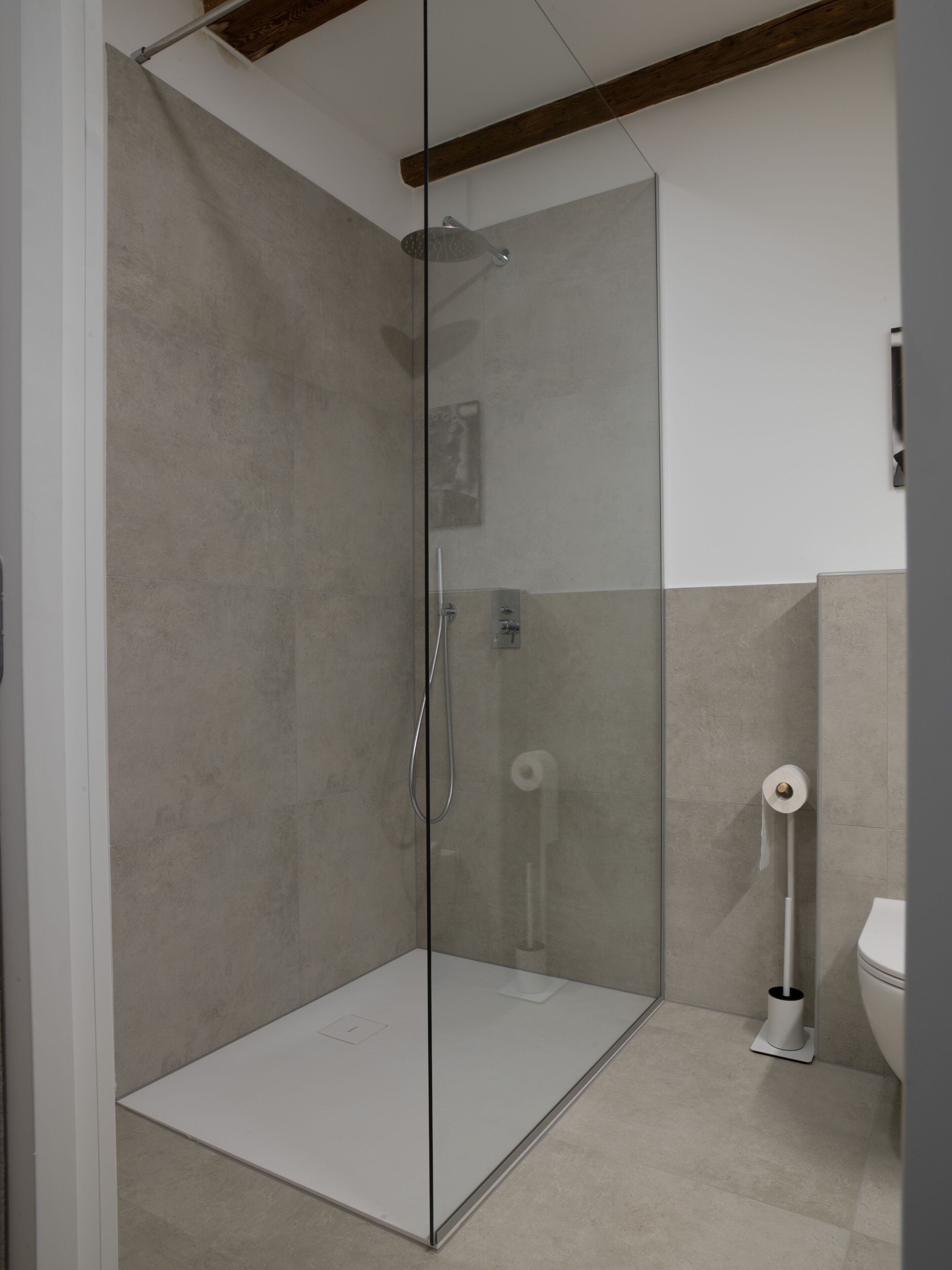 Una ducha moderna con puerta de vidrio, un inodoro y un dispensador de toallas en un baño.