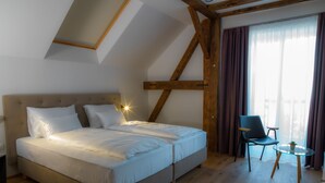 Een slaapkamer met een groot bed, een stoel, een klein tafeltje en een raam met gordijnen.
