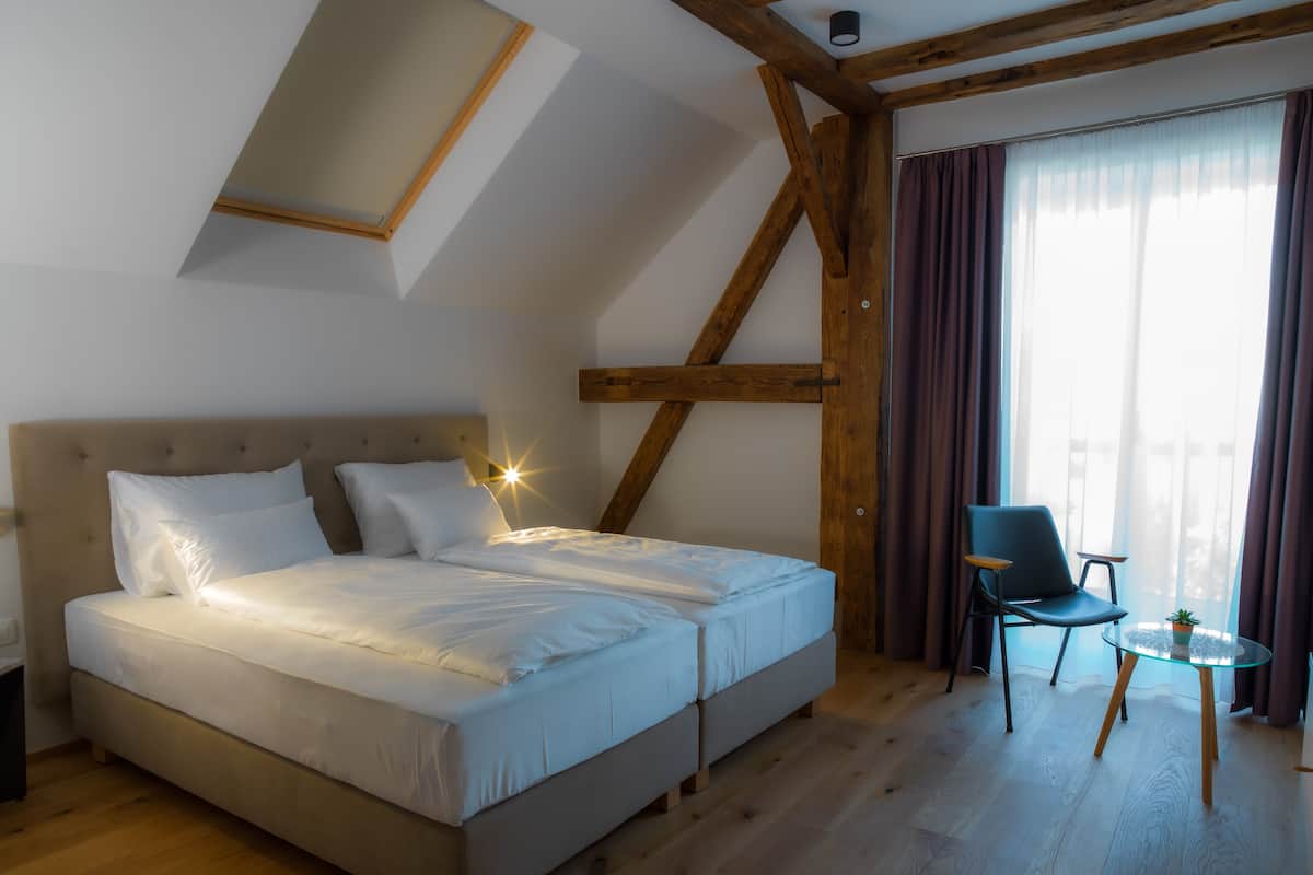Une chambre avec un grand lit, une chaise, une petite table et une fenêtre avec des rideaux.