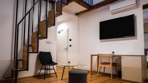 Een moderne kamer met een houten trap, een flatscreen televisie, een klein tafeltje en een bureau met stoel.