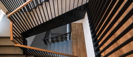 Una escalera moderna con barandillas de madera y metal, que conduce a un rellano con una lámpara.