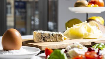 Una tabla de quesos con una variedad de tipos de queso y acompañamientos, incluyendo un huevo entero, un tazón de azúcar y algunas verduras.