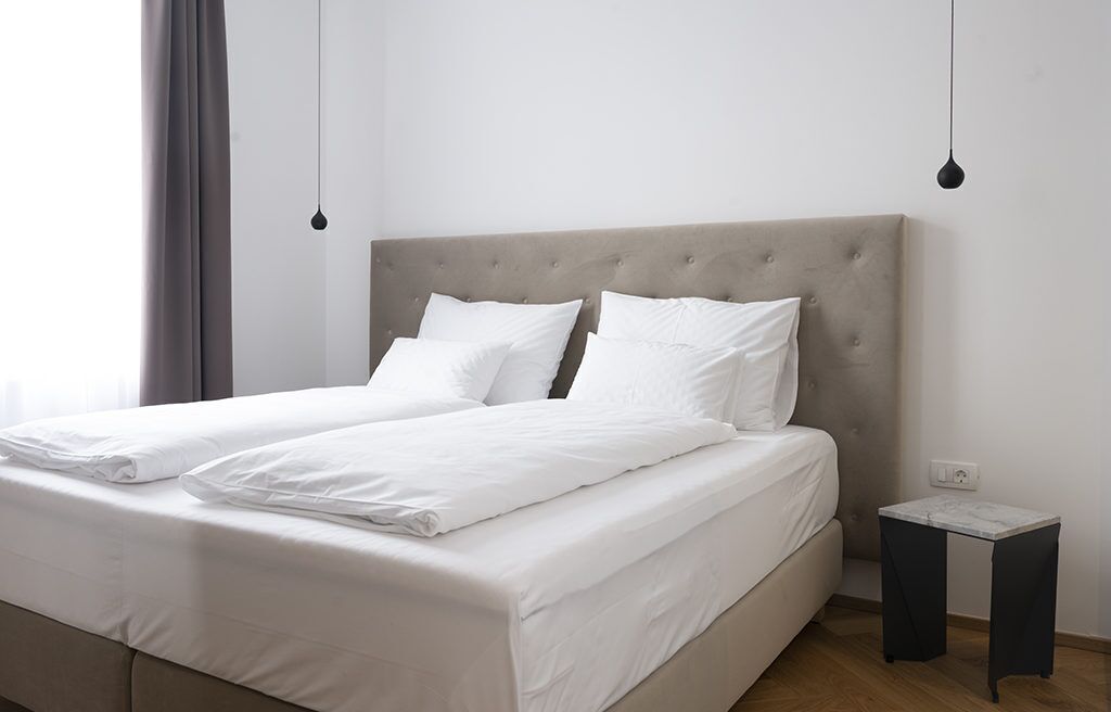 Un lit bien fait, avec du linge de lit blanc et des oreillers, une tête de lit capitonnée et une petite table de chevet avec un plateau en marbre.