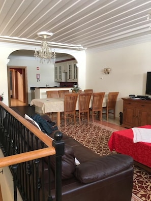 A dining area with a table and chairs, a kitchen in the background, and a staircase with a railing.
