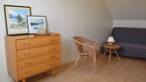 A room with a wooden dresser, a wicker chair, a small round table with a lamp, and a grey sofa. - Self catering accomodation CHEZ GERARD, CHAUMONT sur LOIRE, ideal for a family or group of friends (Chaumont sur loire)