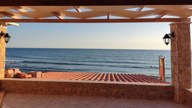 Ein überdachter Außenbereich mit Blick auf das Meer, Steinpfeilern und einem Kachelboden.