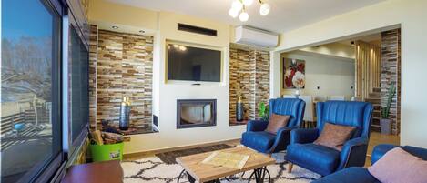Una sala de estar con chimenea, sillones azules, un sofá y un ventanal grande.