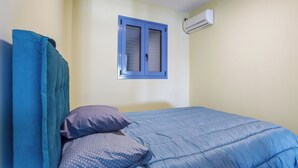 Ein Schlafzimmer mit einem Bett, einem Fenster mit blauen Rollläden und einer Klimaanlage an der Wand.