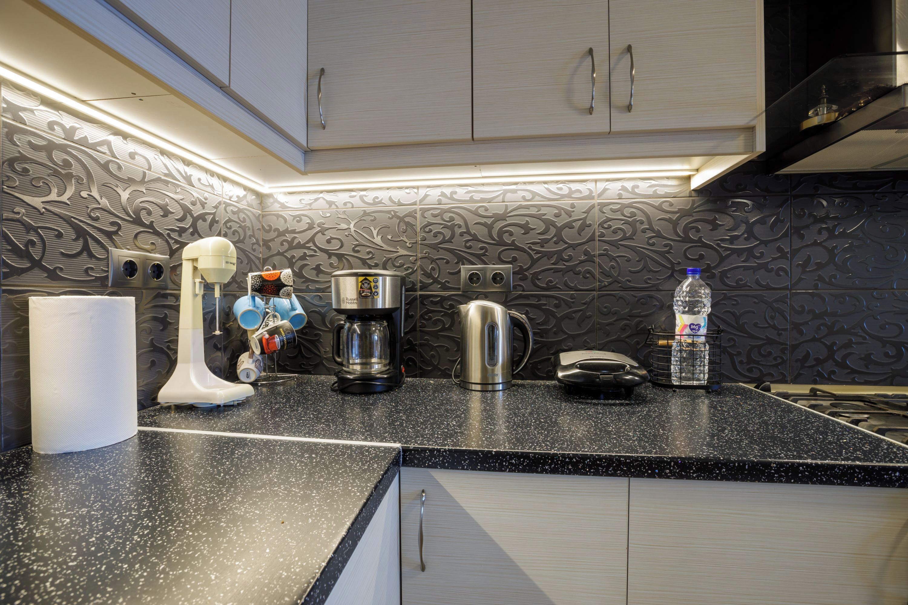 A kitchen with a black countertop, white cabinets, and a decorative backsplash.