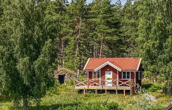 A red cabin with a wooden deck, surrounded by dense forest. - 2 bedroom lovely home in Vikbolandet (Vikbolandet)