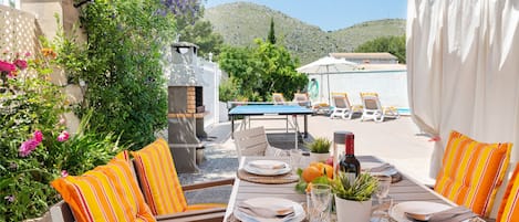 An outdoor dining area with a table set for two, surrounded by striped cushions and a pergola overhead.