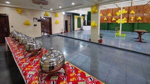 Un salón espacioso con una larga mesa cubierta con un mantel estampado, varias ollas de metal para servir y globos amarillos en las paredes.