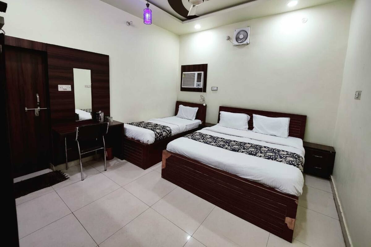 A hotel room with two beds, a desk, a mirror, a ceiling fan, and a wall-mounted air conditioner.