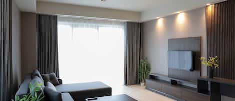 A modern living room with a sectional sofa, a coffee table, a flat-screen TV mounted on the wall, and a potted plant.