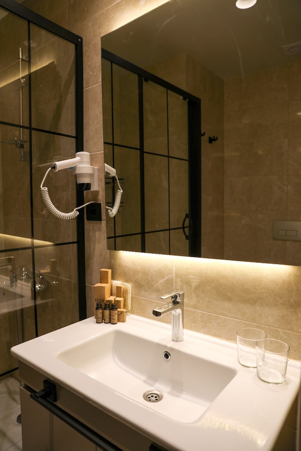 A modern bathroom with a white sink, a mirror, and a hairdryer mounted on the wall. - Hotel 54 (Serdivan)