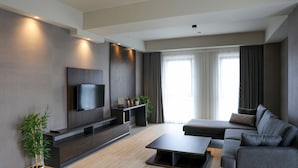 Una sala de estar moderna con un televisor de pantalla plana grande montado en la pared, un sofá de color oscuro, una mesa de centro y una planta en maceta.