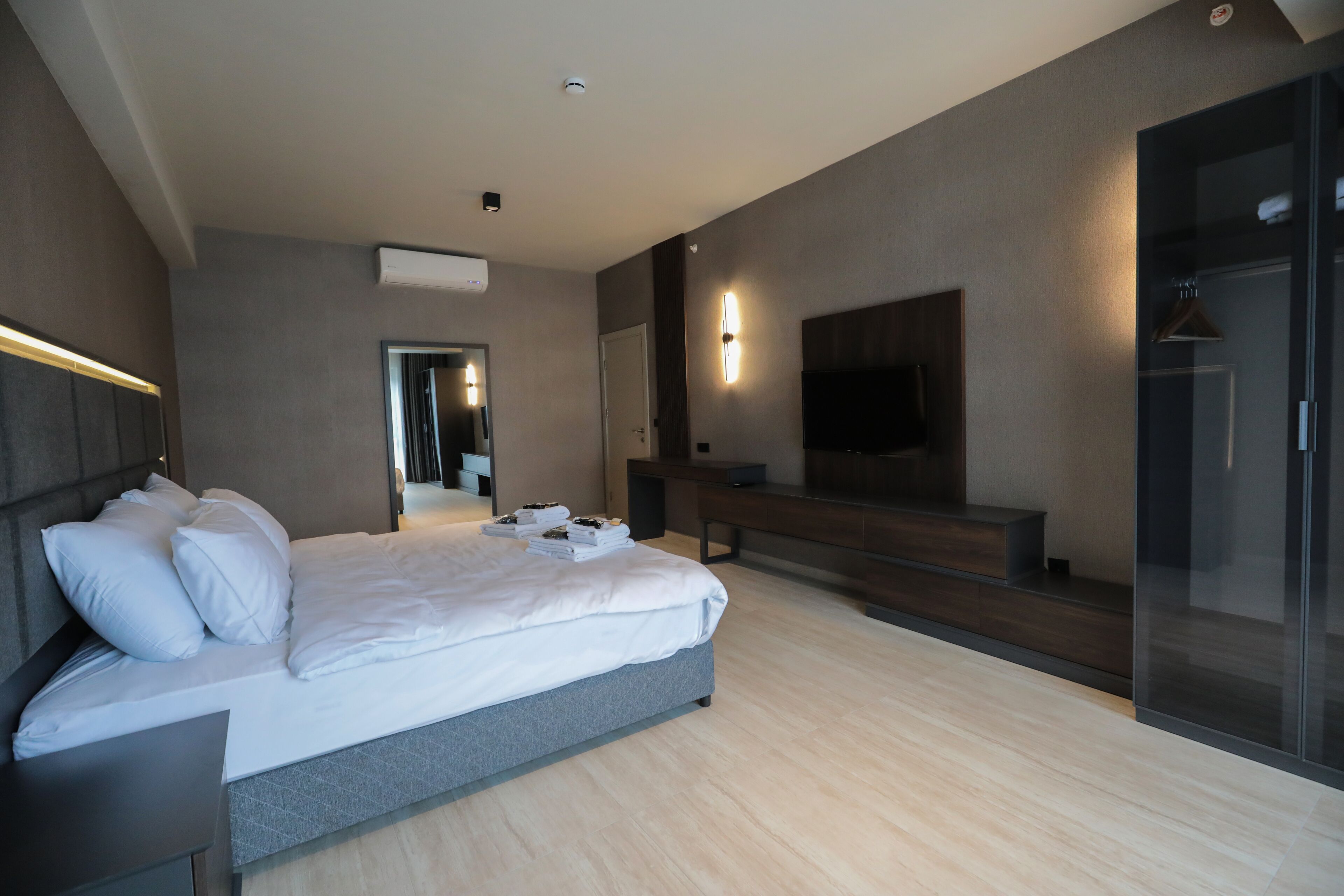 Quarto de hotel moderno com uma cama grande, televisão de tela plana, box de vidro para o chuveiro e um banco embutido.