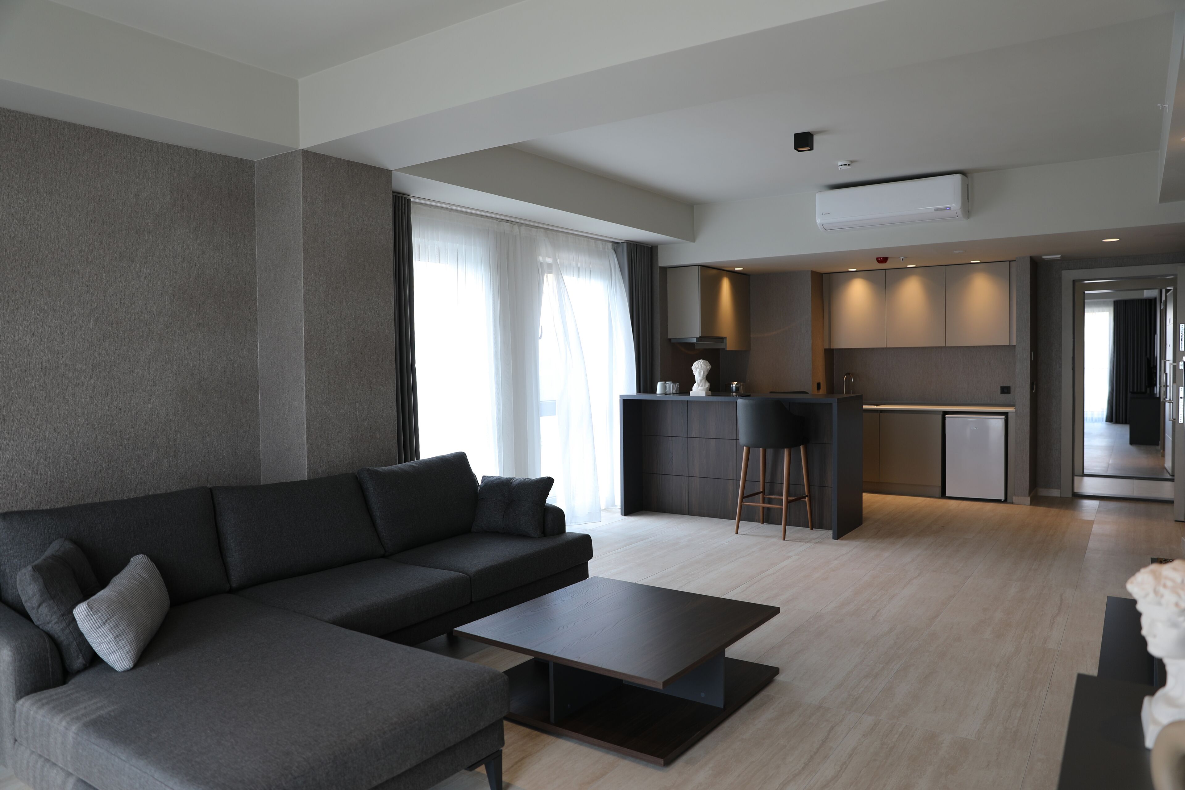 Una sala de estar moderna con un sofá seccional gris, una mesa de centro y una zona de cocina con barra y isla.