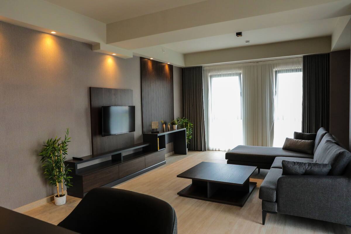 A modern living room with a flat-screen TV, dark sofas, a coffee table, and a wooden floor.