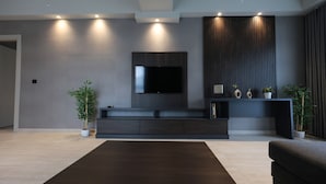 Una sala moderna con un televisor de pantalla plana montado en una pared oscura, un mueble de entretenimiento oscuro debajo y una gran mesa de centro oscura.