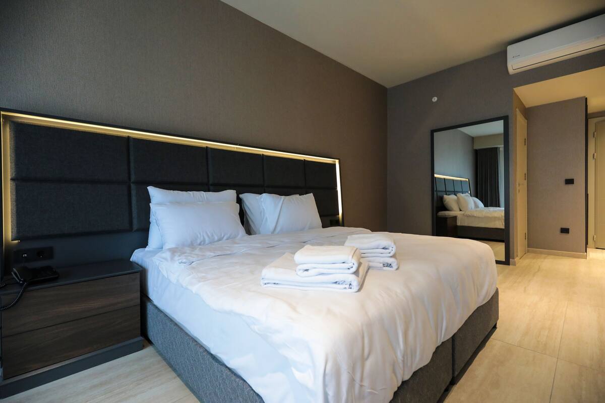 A modern hotel room with a large bed, a bedside table, a nightstand, and a mirror.