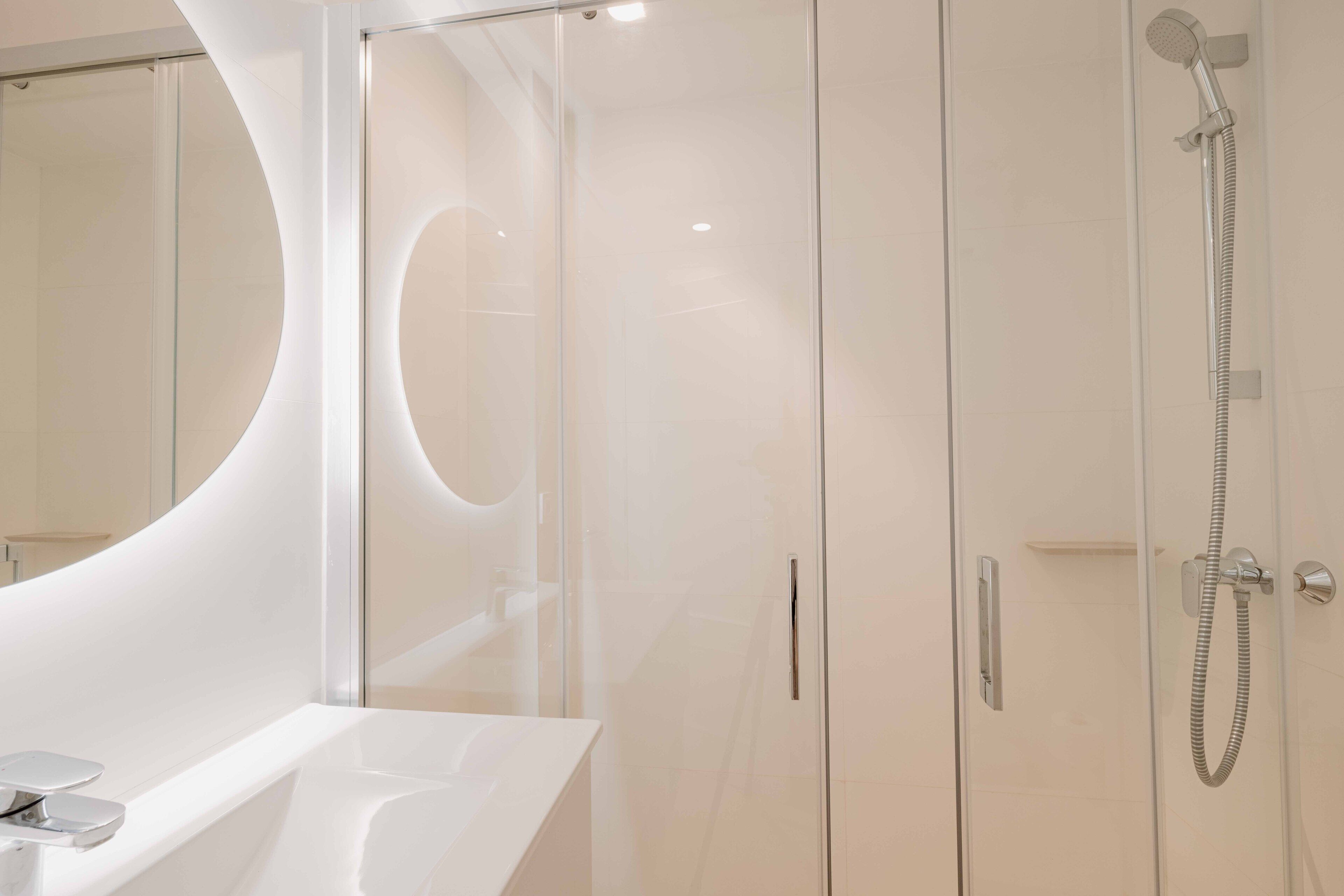 A modern bathroom with a glass shower enclosure, a white sink, and a large mirror.