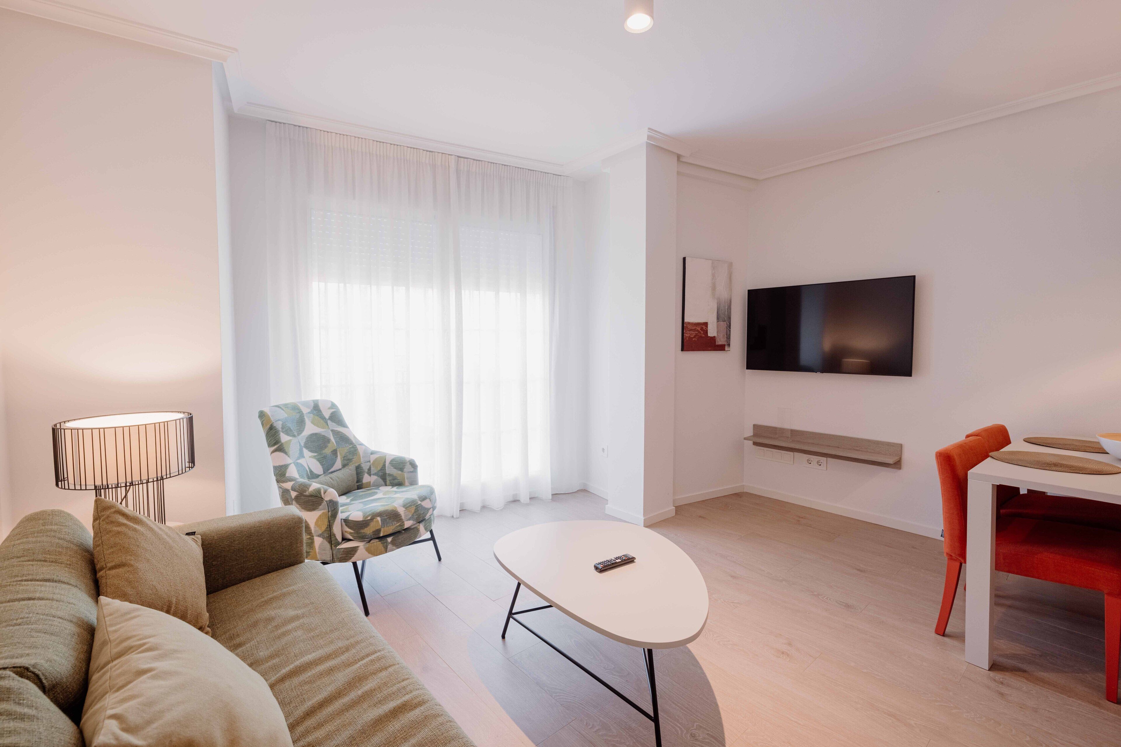 A modern living room with a sofa, a coffee table, a TV, and a dining area with a table and chairs.