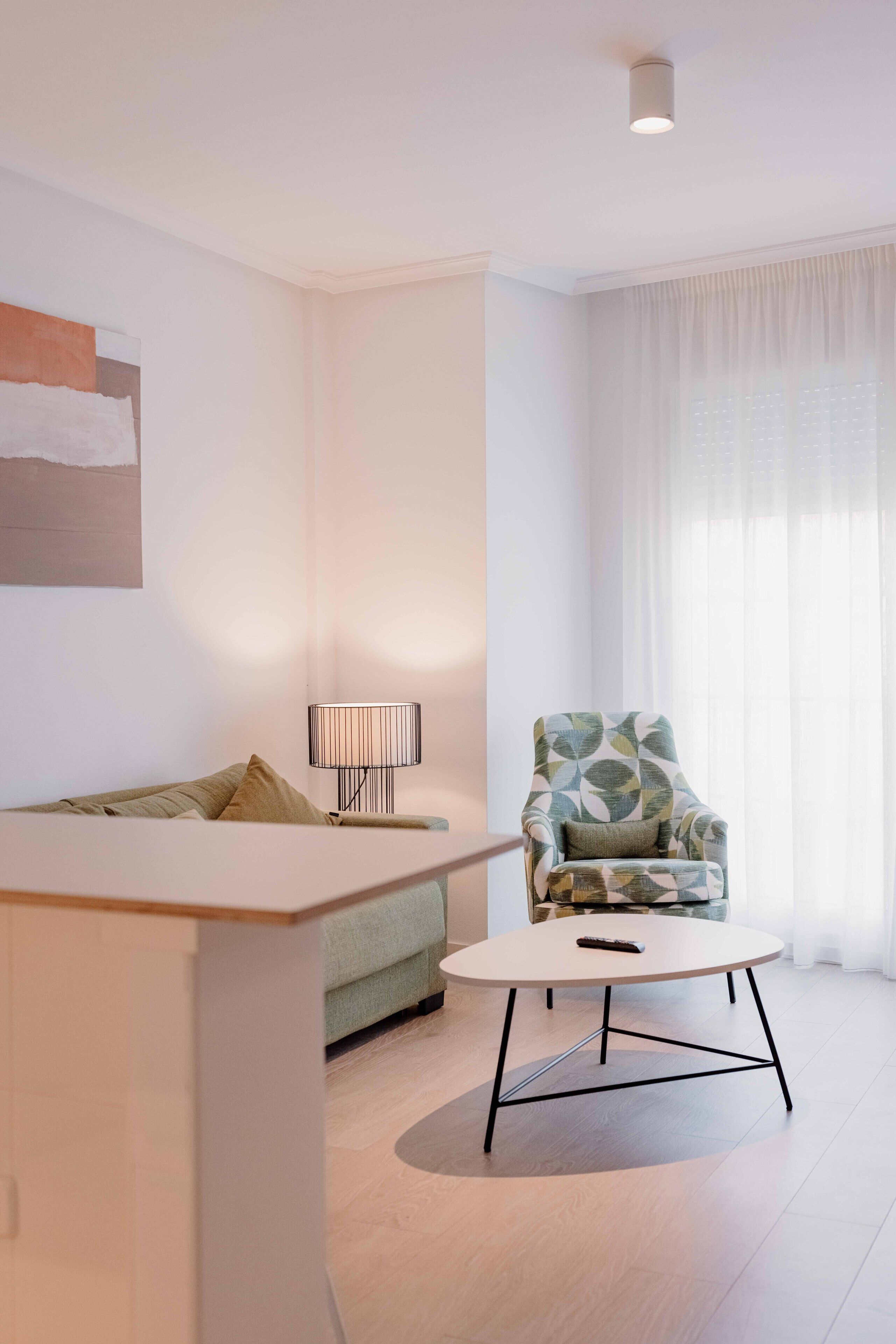 A modern living room with a sofa, a round coffee table, a patterned armchair, and a floor lamp.