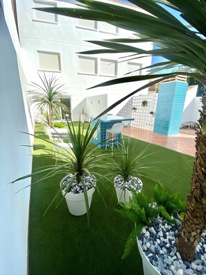 Un espacio exterior moderno con césped artificial, plantas en macetas y una estructura de azulejos azules.