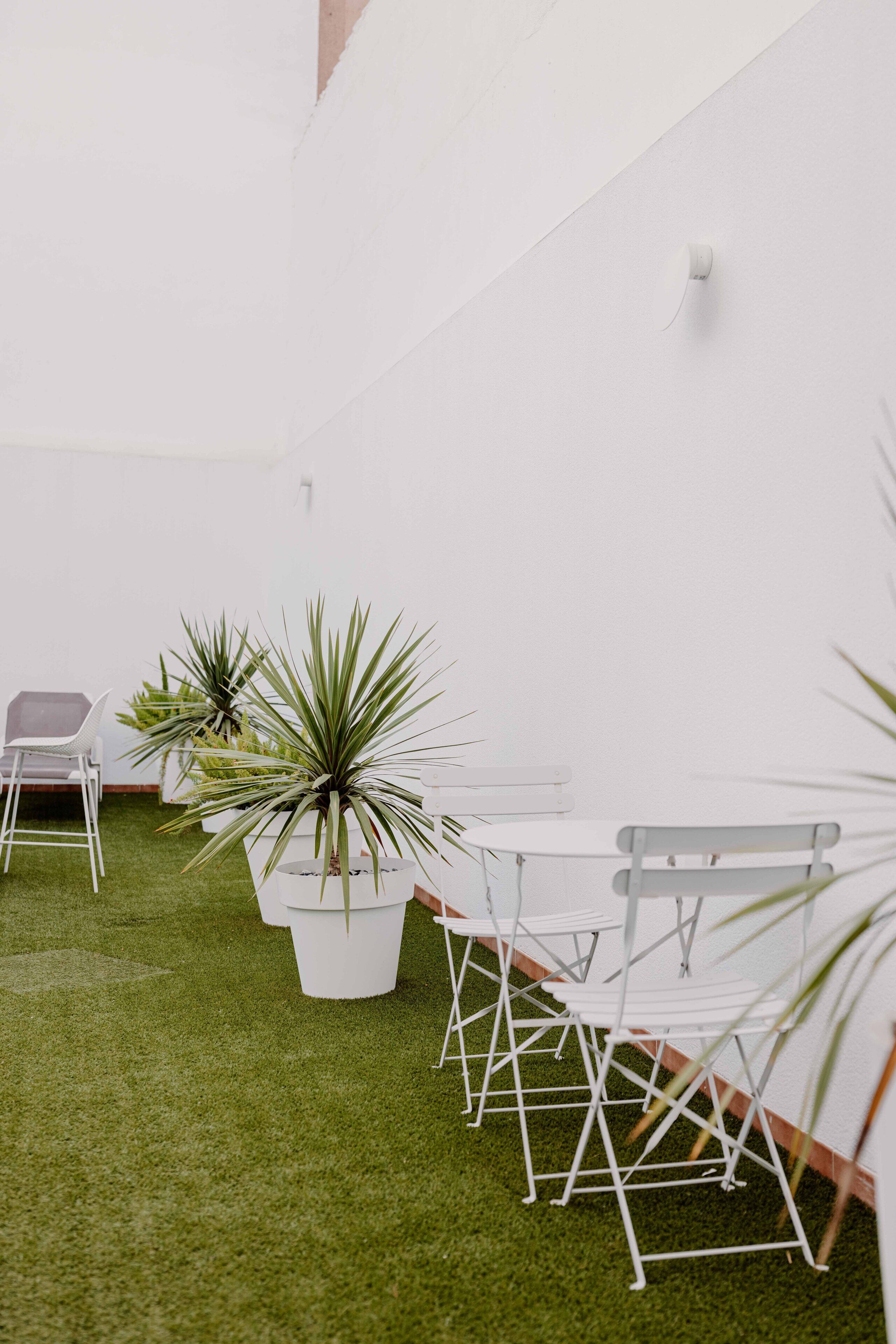 Un espacio interior blanco con césped artificial, muebles blancos y plantas en macetas.