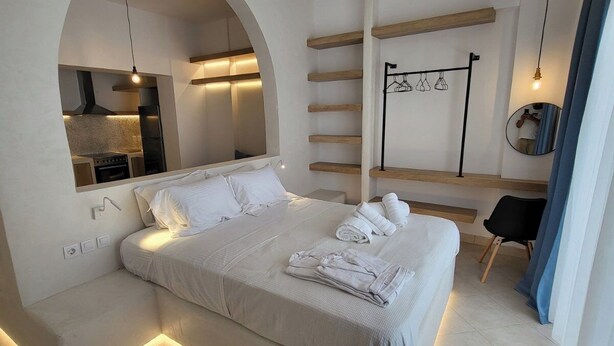 Quarto moderno com cama grande, janela arqueada, cozinha planejada e espelho.
