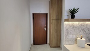 Um corredor com porta de madeira, guarda-roupa de madeira, bancada branca com planta e painel de cozinha salpicado.