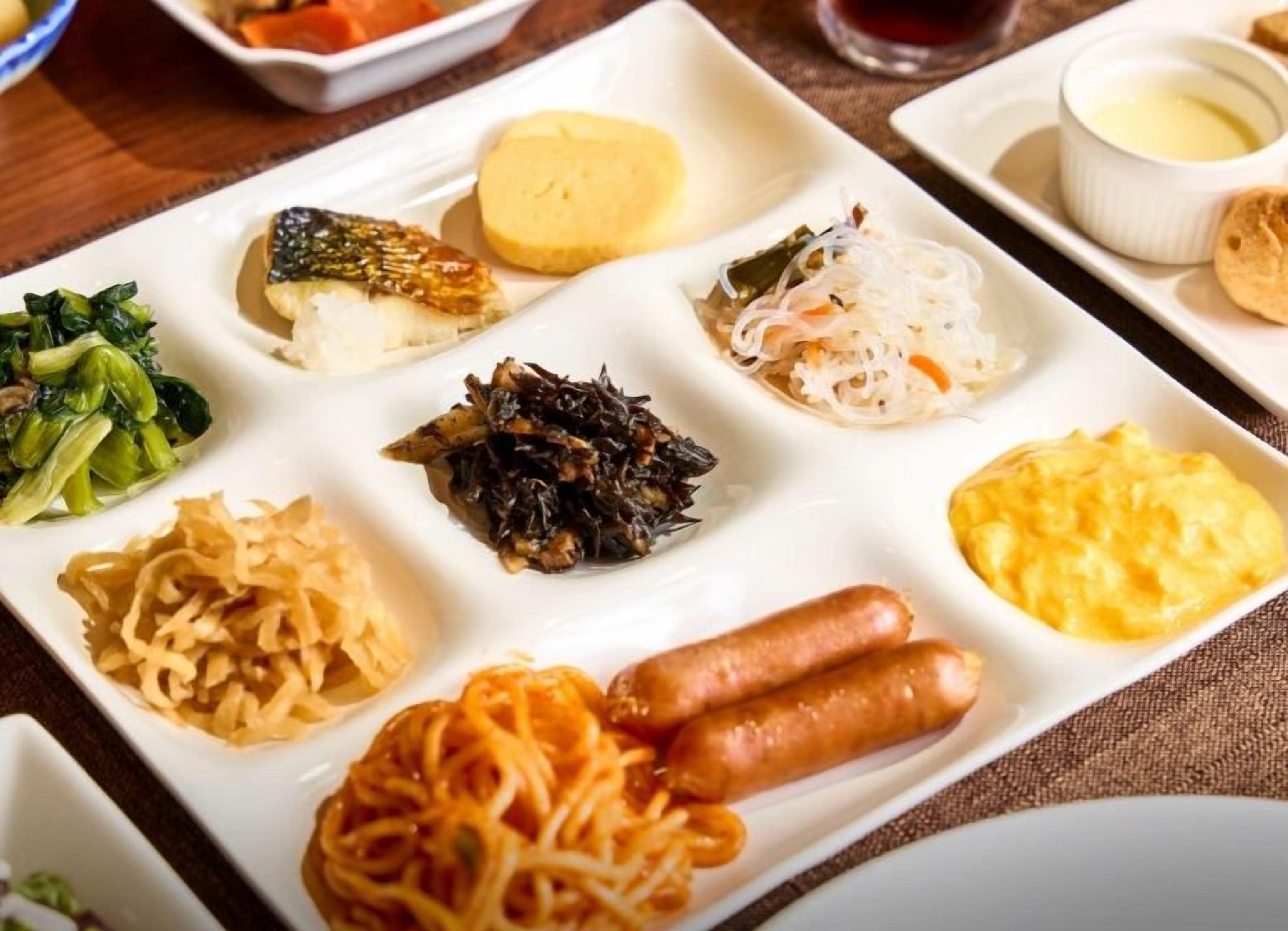 Una variedad de platos en un plato blanco, incluyendo fideos, verduras y salchichas.