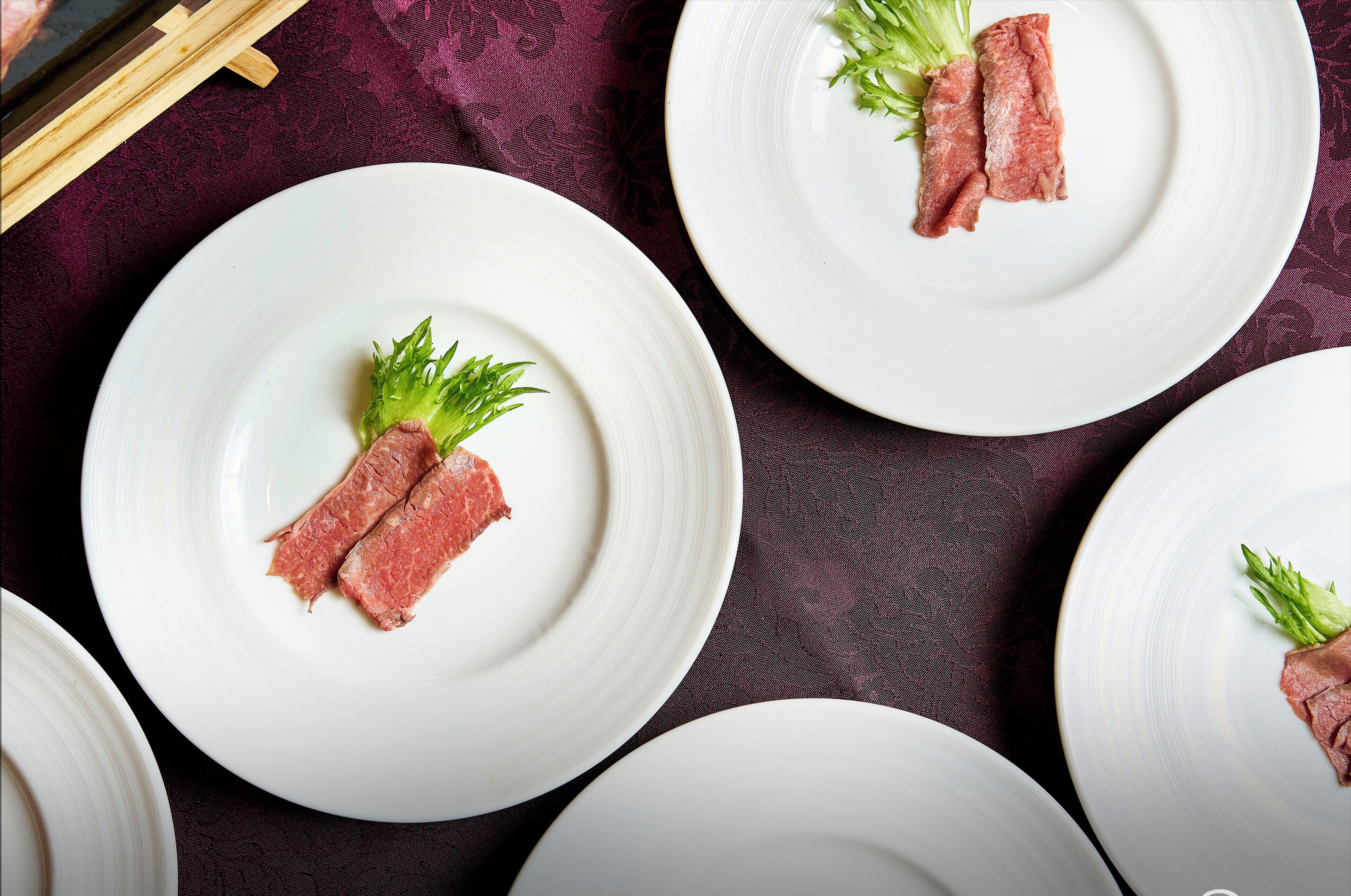 A table with white plates, each with a piece of meat and a green garnish.