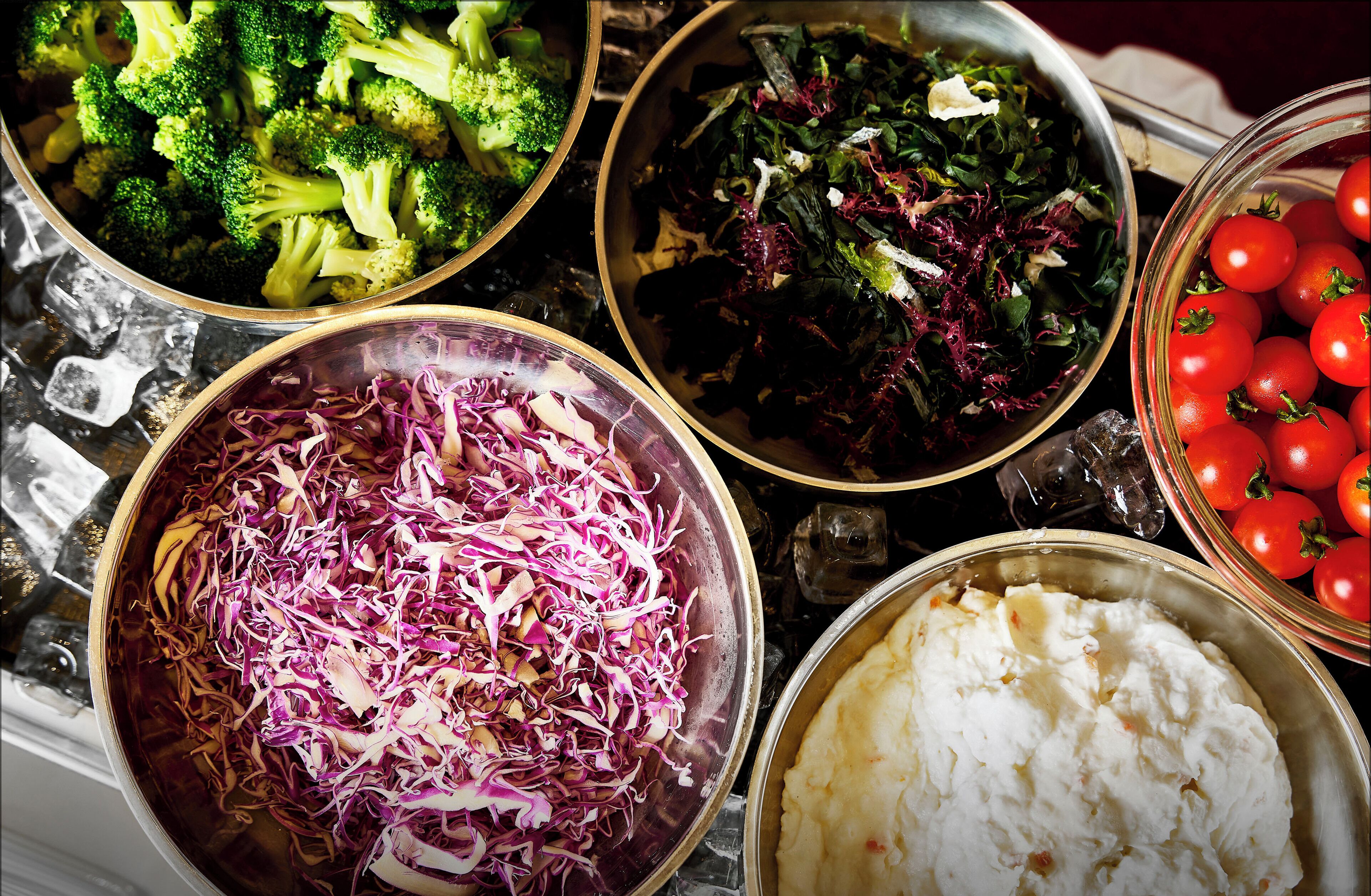 A variety of food items including broccoli, coleslaw, mixed greens, and cherry tomatoes.