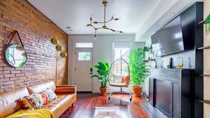 A modern living room with a brick wall, leather sofa, hanging light fixture, and a fireplace.