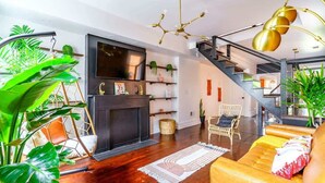 A modern living room with a fireplace, wooden flooring, a sofa, and a staircase.