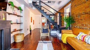 A modern living room with a staircase, wooden floors, a sofa, and a fireplace.