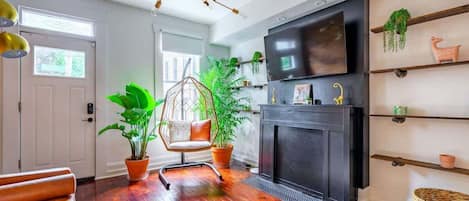 A modern living room with a fireplace, a television, and a variety of plants.